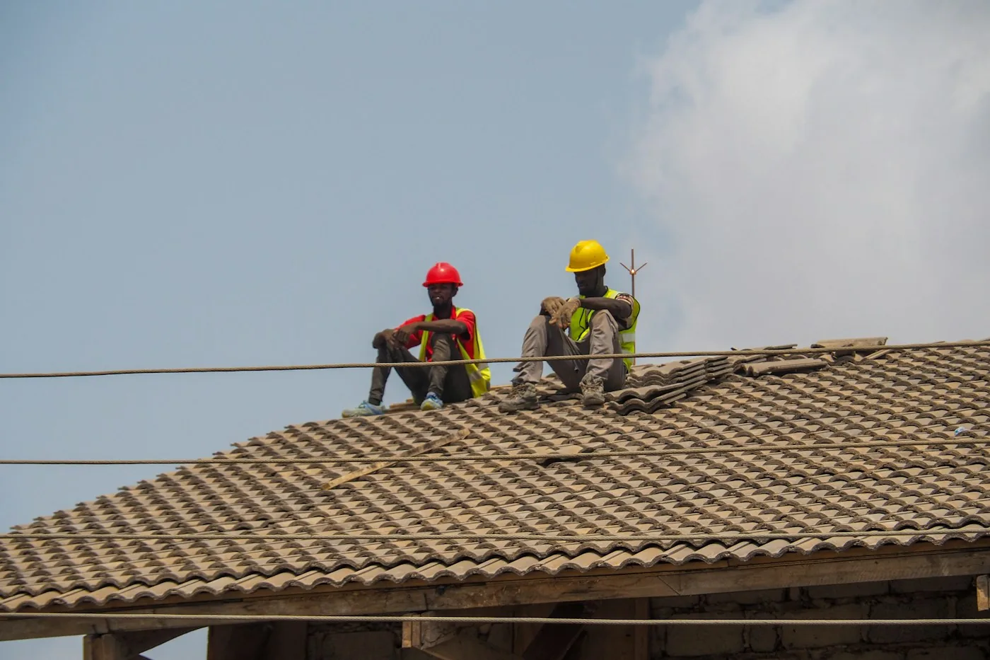 Deux ouvriers en gilets et casques de sécurité en pause sur une toiture de chantier