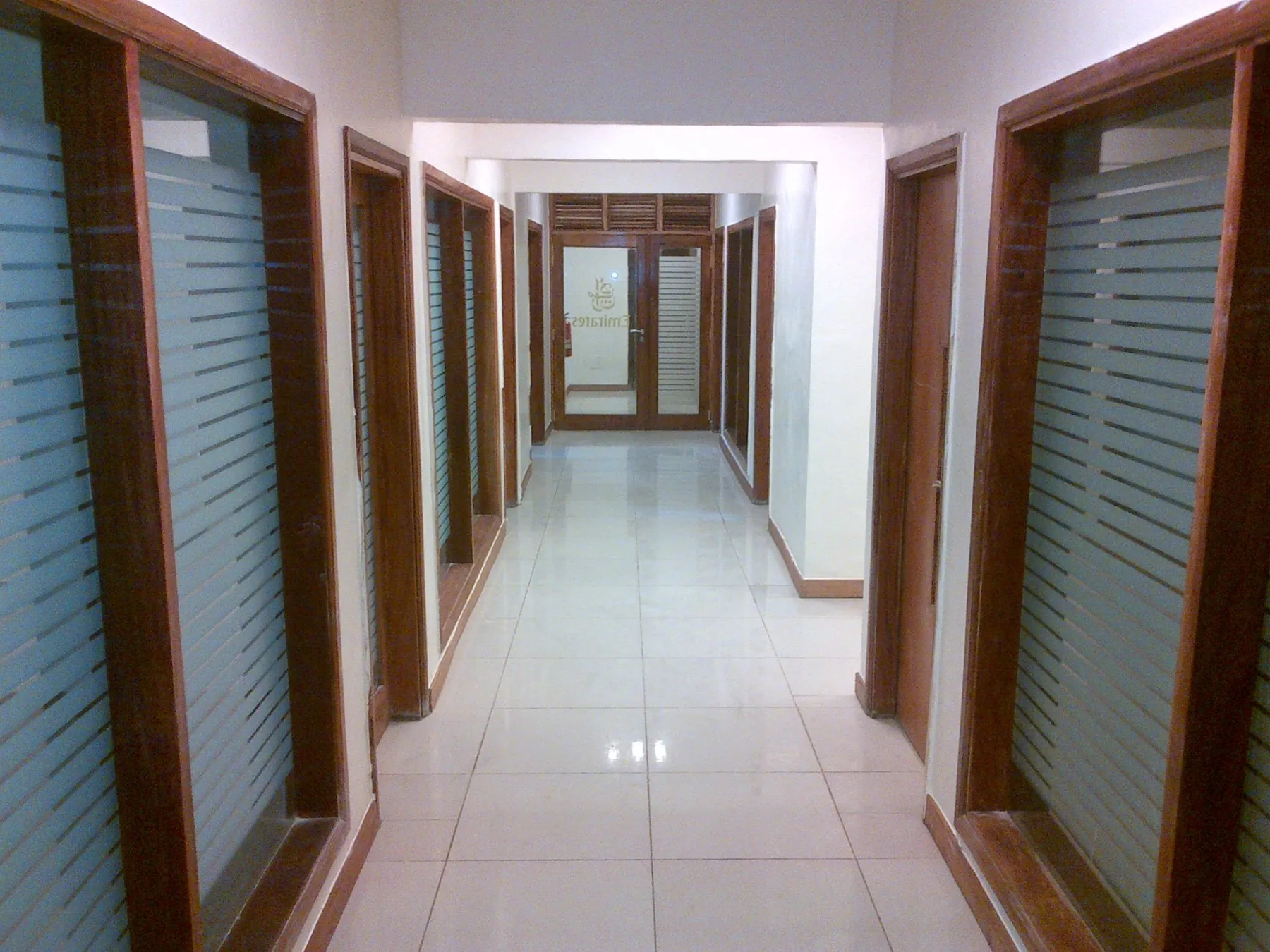 Long couloir aux huisseries en bois et cloisons vitrées dépolies, aménagement de bureaux
