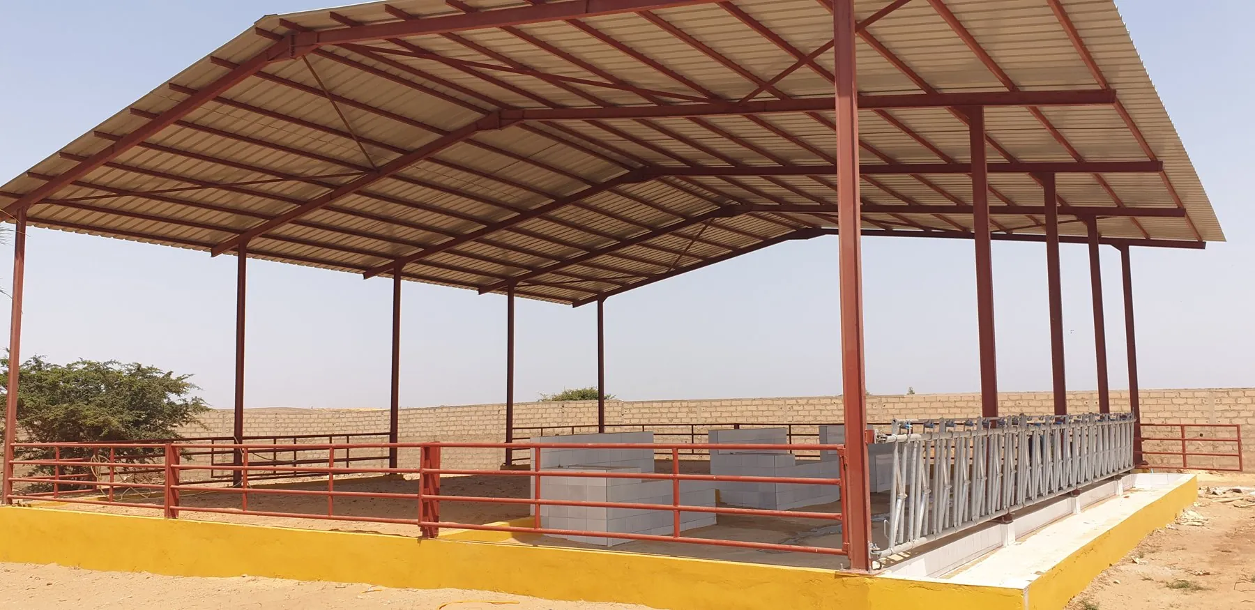 Red steel structure of a cattle building with corrugated roof and tiled trough