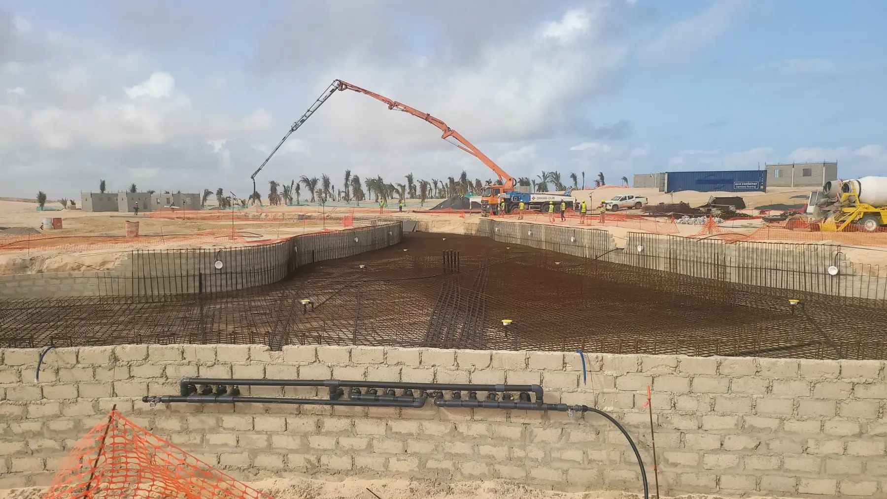 Chantier de bassin ferraillé avec camion-pompe à béton et équipes